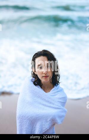 Young woman wrapped in white towel against sea at Praia da Ursa, Lisboa, Portugal Stock Photo