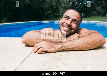 Smiling handsome wet young man looking away while relaxing in swimming pool Stock Photo