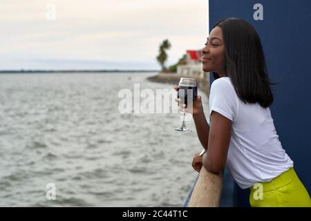 Happy young woman with glass of red wine looking at the sea Stock Photo