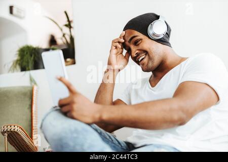 Portrait of smiling man using mini tablet and headphones at home Stock Photo