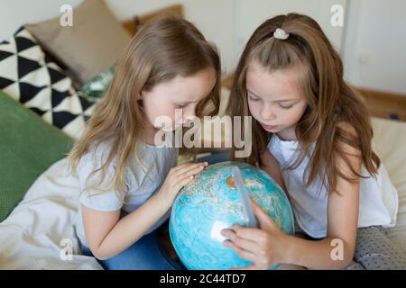 Two sisters sitting together on bed looking at globe Stock Photo