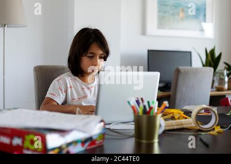 Portrait of boy sitting at table in the living room using laptop Stock Photo