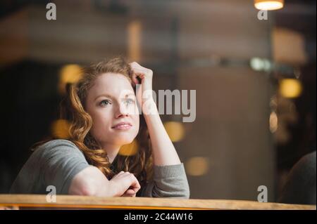 Thoughtful woman leaning on table seen through glass window in coffee shop Stock Photo