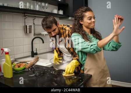 Young multiethnic couple is cleaning their kitchen. Woman is lazy and man is angry. Stock Photo