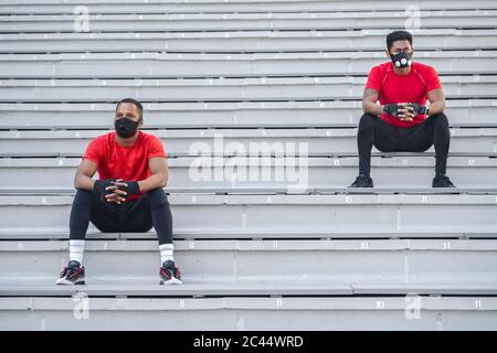 Two sportsmen wearing masks sitting on stairs Stock Photo