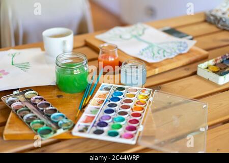 Watercolor paints with water and paintbrushes on wooden table home Stock Photo