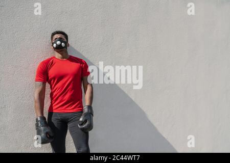 Portrait of a sportsman wearing face mask and boxing gloves at a wall Stock Photo