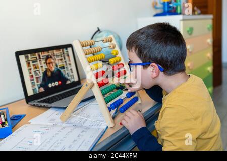 Boy with abacus at desk while teacher on video call during pandemic homeschooling Stock Photo