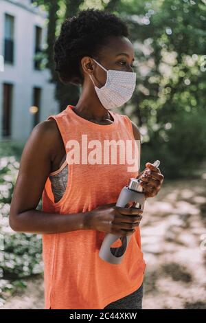 Portrait of sportive young woman with  flask wearing protective mask Stock Photo