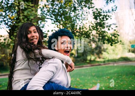 Cheerful mother piggybacking daughter while standing in park Stock Photo