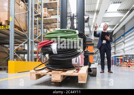 Businessman instructing worker on forklift in high rack warehouse Stock Photo