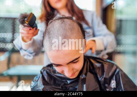 Mother shaving teenage son's head with electric razor at home Stock Photo