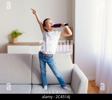 Girl Singing Holding Hairbrush Like Microphone Standing On Sofa Indoor Stock Photo