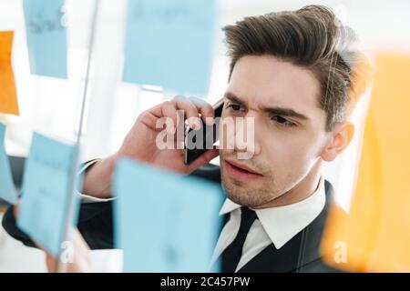 Image of focused caucasian businessman wearing suit talking on cellphone while working in office Stock Photo