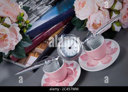 Silver alarm clock like an airplane, books and rose flowers teacups. Spring time change. Stock Photo