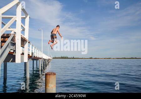 A young boy jumps from the 1.8km long Busselton Jetty (the longest timber-piled jetty in Australia) into Geographe Bay in Western Australia Stock Photo