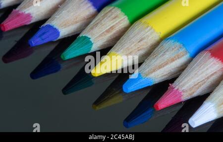 Coloured pencil crayons on a black reflective surface. Rainbow of different coloured pencils for school Stock Photo