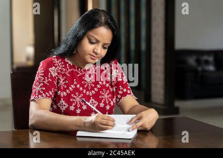 An Indian woman writing notes in her diary, asian woman sitting in her living room planning in her diary Stock Photo