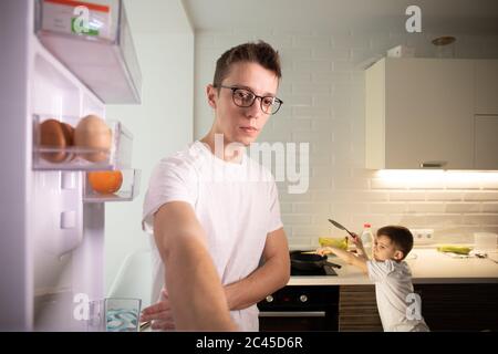 Camera Inside Kitchen Fridge: Man Opens Fridge Door, Looks inside. Stock Photo