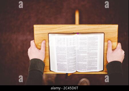 Closeup shot of a wooden speech stand with an opened book and person hands holding it Stock Photo