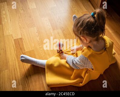 The original Kendama. An ancient, traditional, wooden Japanese skill toy for children. Has three cups, spike and ball. A little girl dressed in yellow Stock Photo