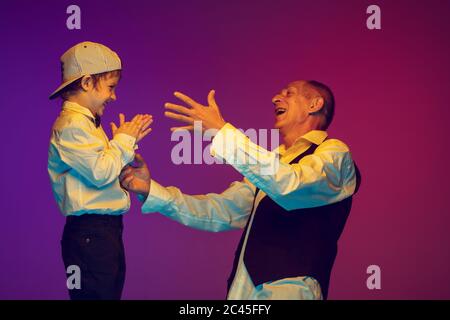 Senior man having fun and spending time together with boy, grandson in neon light. Joyful elderly lifestyle, family, childhood, communication concept. Enjoying playing, laughting. Copyspace. Stock Photo