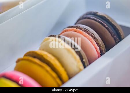 Close up view - row of bright colorful macarons or macaroons cakes for sale in box at candy shop, market, cafe or bakery. Dessert, biscuit, sweet food Stock Photo