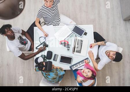 Group of young men and women around a table, looking upwards, using keywords and laptops Stock Photo