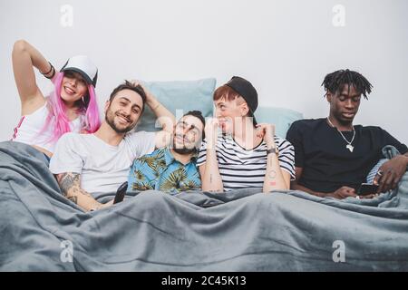 Group of young men and women lying in a bed, looking at camera. Stock Photo