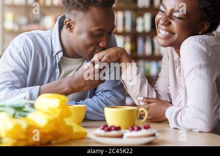 Handsome African American guy kissing his girlfriends hand at coffee shop Stock Photo