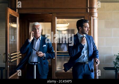 Two businessmen leaving hotel lobby, using mobile phones. Stock Photo