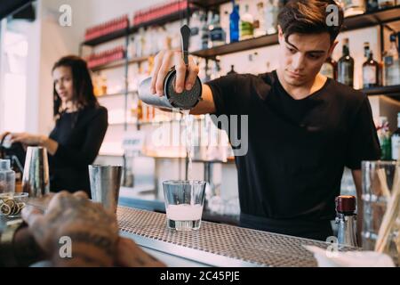 Young woman and man wearing black clothes standing behind bar counter, preparing drinks. Stock Photo