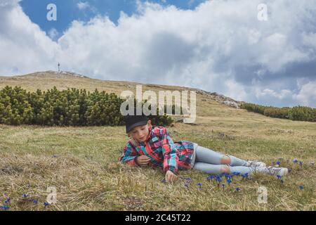 Young girl laying on meadow picking blue bladder gentian in alpine mountain environment Stock Photo
