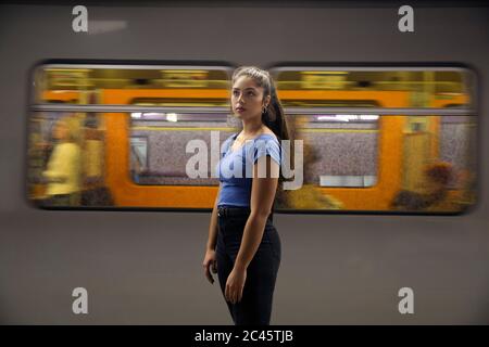 Young woman with long brown hair standing in front of commuter train on railway station platform. Stock Photo