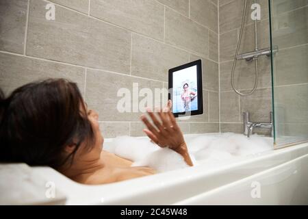 Woman sitting in bathtub, having foam bath and using digital tablet during Coronavirus crisis. Stock Photo