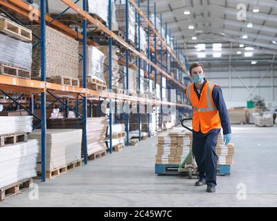 Man wearing surgical face mask and high visibility vest working in a large warehouse.
