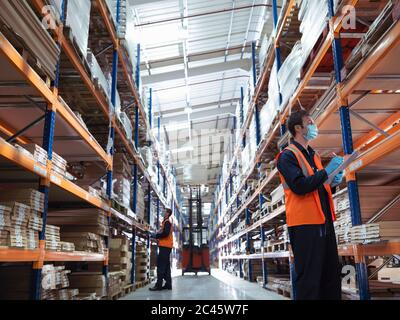 Man wearing surgical face mask and high visibility vest working in a large warehouse.