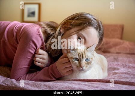 Portrait of girl and white and ginger cat lying on bed. Stock Photo