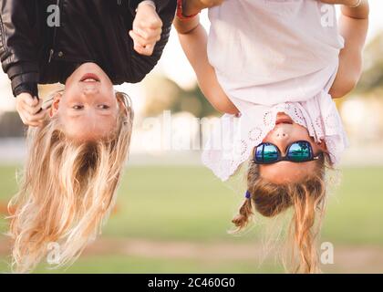 Two young girls, age 8-12, hanging upside down on outdoor fitness device Stock Photo