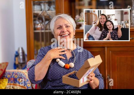 Senior woman holding birthday present during online celebration with her family during Coronavirus lockdown. Stock Photo