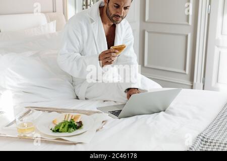Man using laptop and having toast in suite Stock Photo