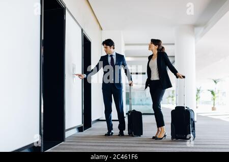 Businessman and businesswoman with wheeled luggage waiting for hotel escalators Stock Photo