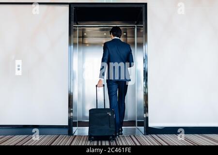 Businessman with wheeled luggage entering hotel lift Stock Photo
