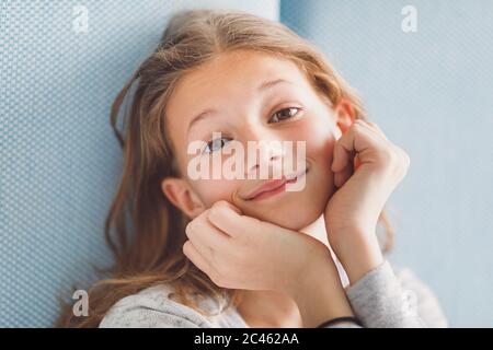 Light and airy portrait of young girl smiling at camera in front of blue background Stock Photo