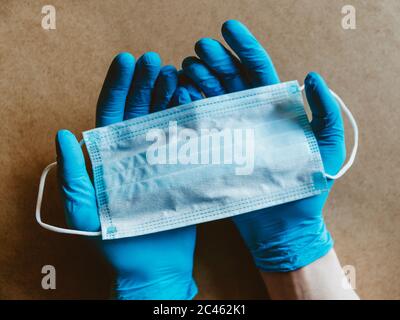 Hand in blue rubber gloves holds a medical mask. Health care and antivirus protection concept, top view. Stock Photo