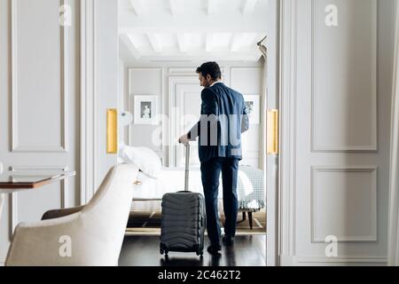 Businessman with wheeled luggage in suite Stock Photo