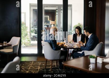 Two businessmen and woman having working lunch in hotel restaurant Stock Photo