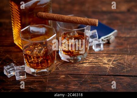 Bottle of whiskey with two glasses and cuban cigar placed on rustic wooden table Stock Photo