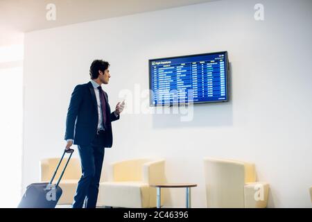 Businessman with wheeled luggage checking departure board Stock Photo