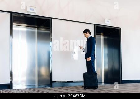 Businessman with wheeled luggage by hotel lift Stock Photo